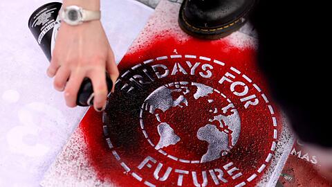 Eine Klimaaktivistin sprüht während einer Kundgebung ein Logo der Bewegung Fridays For Future auf ein Transparent.