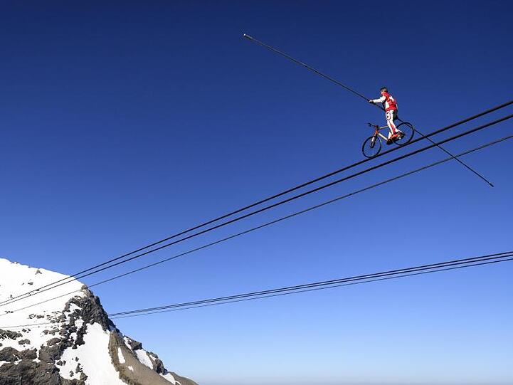 Der Schweizer Drahtseilkünstler Freddy Nock mit einem Fahrrad auf einem Seil einer Seilbahn.