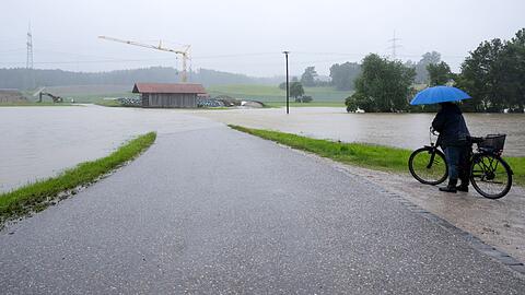 Eine Frau steht mit ihrem Fahrrad an einer überspülten Straße.