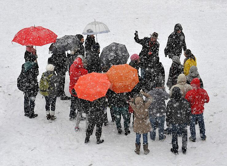 Eine Touristengruppe schützt sich auf dem Marienplatz mit Schirmen vor dem Schnee. Der Touristenführer hält der weißen Pracht aber tapfer stand.