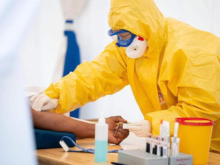 Eine Rettungssanitäterin entnimmt in einem Zelt einem Patienten Blut.