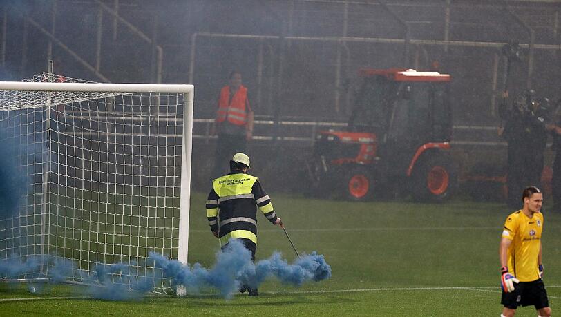 Ein Feuerwehrler entfernt eine Rauchbombe beim kleinen Derby im Grünwalder Stadion Ein Feuerwehrler entfernt eine Rauchbombe beim kleinen Derby im Grünwalder Stadion