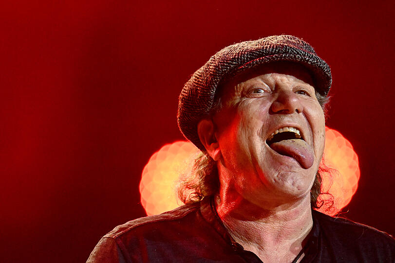 Brian Johnson strahlt mit Schiebermütze und schlichtem Polohemd  Kumpelhaftigkeit pur aus.