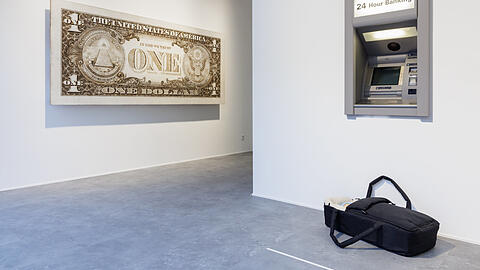 Eine Tragetasche samt Baby steht vor dem Geldautomaten. Hat da jemand sein Kind vergessen, oder spekuliert er oder sie, dass sich ein freundlicher Mitmensch erbarmt und dem „Modern Moses“ ein gutes neues Zuhause schenkt? Was zählt, ist das Geld. Tom Sachs bringt das mit seiner überdimensionalen „One Dollar“-Note prima zum Ausdruck. Eine Tragetasche samt Baby steht vor dem Geldautomaten. Hat da jemand sein Kind vergessen, oder spekuliert er oder sie, dass sich ein freundlicher Mitmensch erbarmt und dem „Modern Moses“ ein gutes neues Zuhause schenkt? Was zählt, ist das Geld. Tom Sachs bringt das mit seiner überdimensionalen „One Dollar“-Note prima zum Ausdruck.