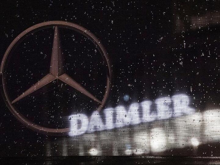 Das Logo der Daimler-AG ist an der Konzernzentrale zu sehen, im Vordergrund ist ein Mercedes-Stern auf einer Flagge abgebildet, die voller Regentropfen ist.