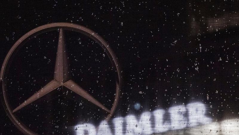 Das Logo der Daimler-AG ist an der Konzernzentrale zu sehen, im Vordergrund ist ein Mercedes-Stern auf einer Flagge abgebildet, die voller Regentropfen ist.