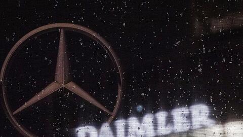 Das Logo der Daimler-AG ist an der Konzernzentrale zu sehen, im Vordergrund ist ein Mercedes-Stern auf einer Flagge abgebildet, die voller Regentropfen ist.
