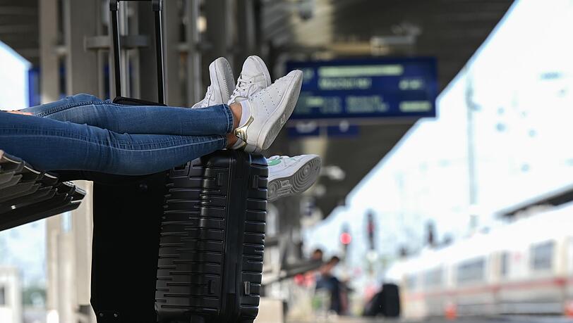 Zwei Reisegäste warten an einem Bahnhof am Gleis.