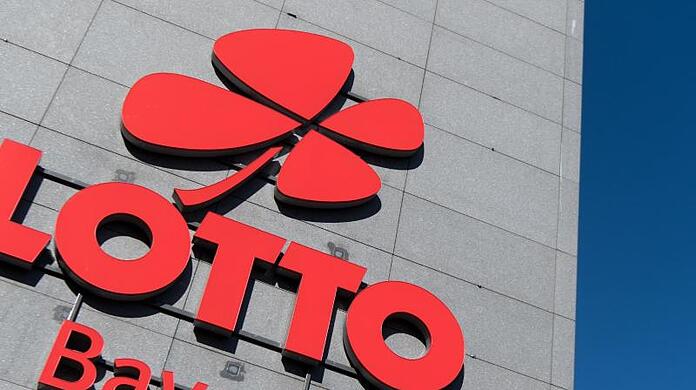 Das Logo und der Schriftzug "Lotto Bayern" sind an dem Firmengebäude der Lottozentrale in München zu sehen.