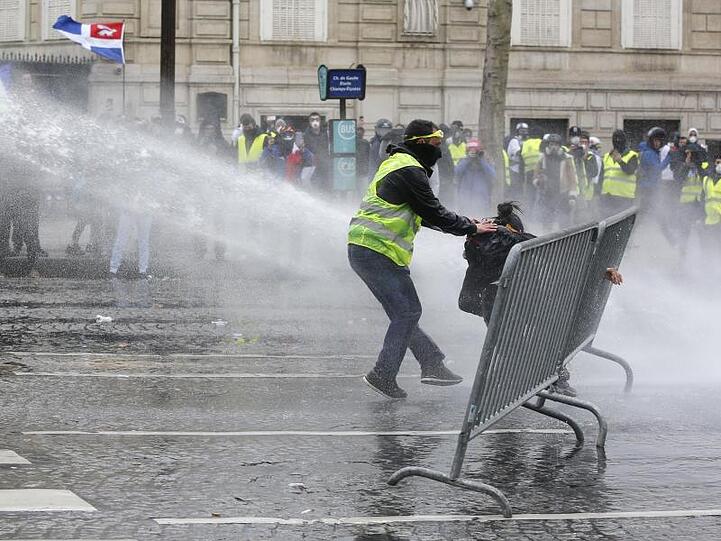Ein Demonstrant eilt einer Demonstrantin zu Hilfe, während Polizisten Wasserkanonen einsetzen.