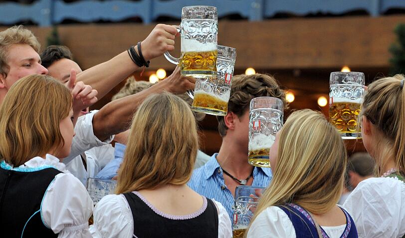 Junge Wiesn-Besucher prosten sich freudig mit ihren Krügen zu.