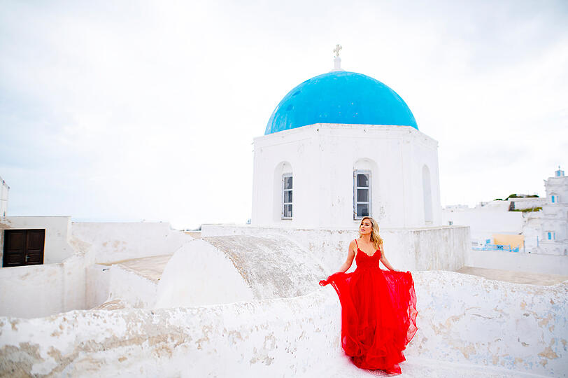 Wei&szlig;e H&auml;user, blaue D&auml;cher: Christina Beier in rotem Kleid vor der klassischen Santorini-Kulisse.
