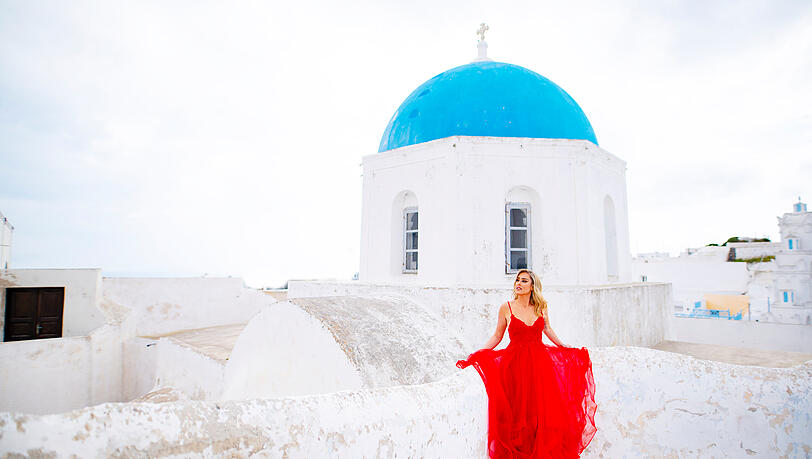 Wei&szlig;e H&auml;user, blaue D&auml;cher: Christina Beier in rotem Kleid vor der klassischen Santorini-Kulisse.