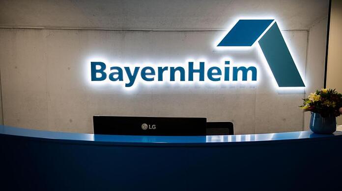 Das Logo der BayernHeim hängt in der Geschäftsstelle hinter einem Tresen.