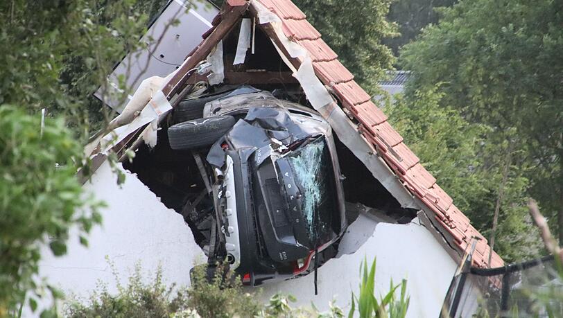 Ein Auto liegt nach einem kurzen Flug seitlich in der Mauer einer Scheune.