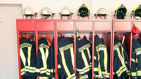 Jacken und Helme der Feuerwehr hängen in einem Schrank. Foto: Bernd Wüstneck/zb/dpa/Symbolbild
