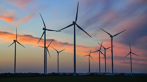 Farbenprächtig leuchten Wolken am Morgenhimmel kurz vor Sonnenaufgang über einem Windpark. (Symbolbild)