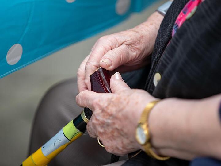 Eine Seniorin sitzt mit ihrem Gehstock im Garten eines Pflegeheims.