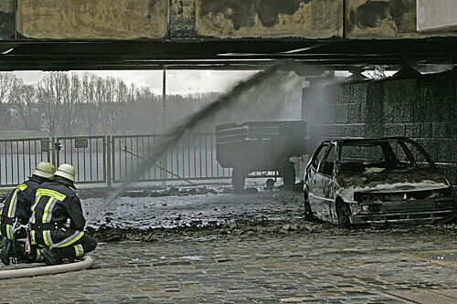 Feuerwehrleute kühlen neben einem ausgebrannten Auto die Stahlkonstruktion der Protzenweiherbrücke über die Donau.