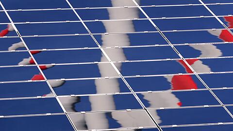 Ein Windrad spiegelt sich in eine Photovoltaik-Anlage eines Solarparks.