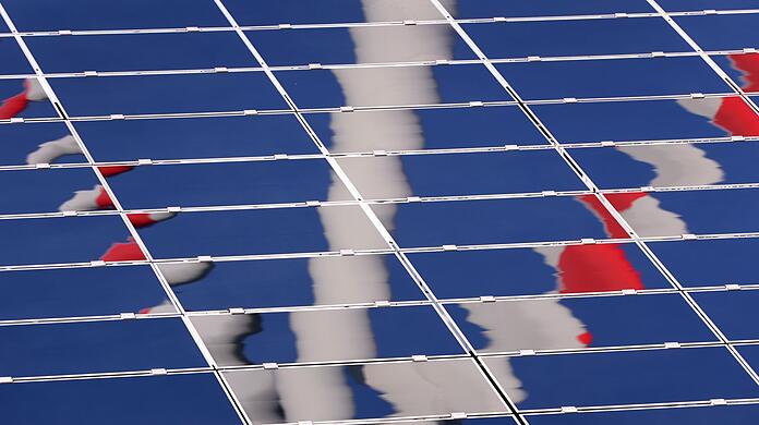 Ein Windrad spiegelt sich in eine Photovoltaik-Anlage eines Solarparks.