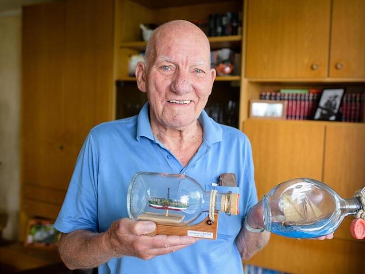 Wilfried Menke, Buddelschiffbauer aus Norddeutschland, hält in seiner Wohnung zwei seiner Buddelschiffe in den Händen. Foto: Matthias Balk
