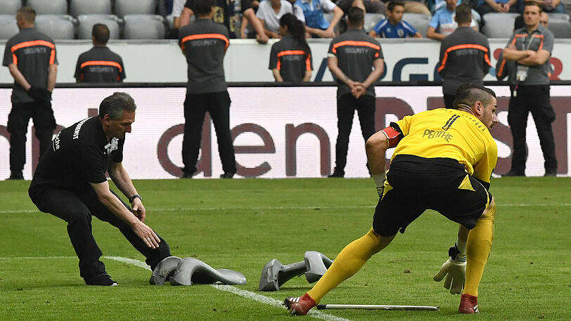 Ein Ordner und Torwart Philipp Pentke von Regensburg heben Sitzschalen auf, die auf das Spielfeld geworfen wurden.