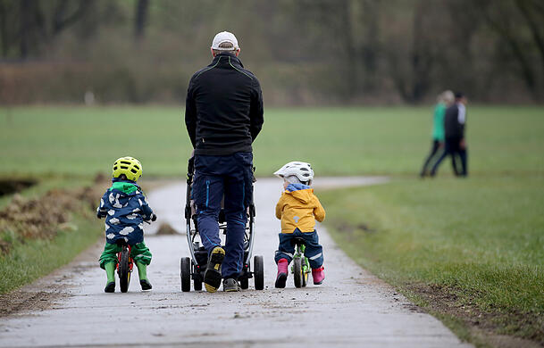 Ein Vater geht mit seinen drei Kindern spazieren.