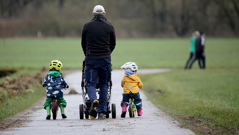 Ein Vater geht mit seinen drei Kindern spazieren.