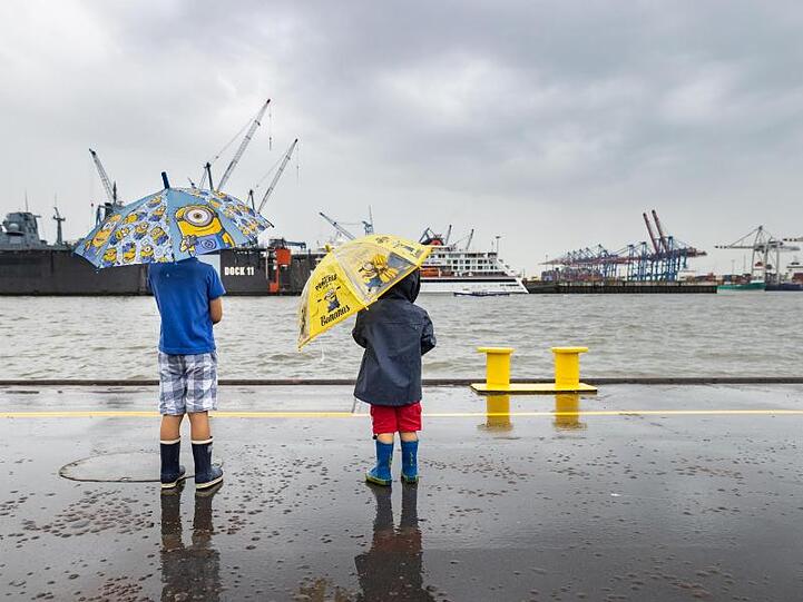 Mit bunten Regenschirmen schützten sich zwei Jungen im Hafen Hamburg vor dem Regen. Nach vielen trockenen, sonnigen Tagen regnet es wieder in der Hansestadt.