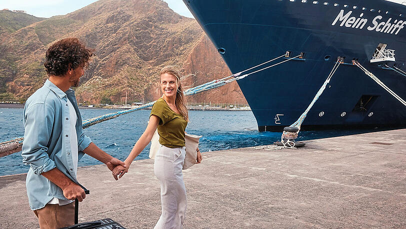 Ein Paar - ohne Kinder - vor einem Kreuzfahrtschiff.  F