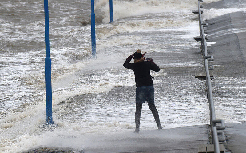 Wellen überspülen den Fähranleger in Dagebüll (Schleswig-Holstein), während eine Frau gegen den Wind kämpft.