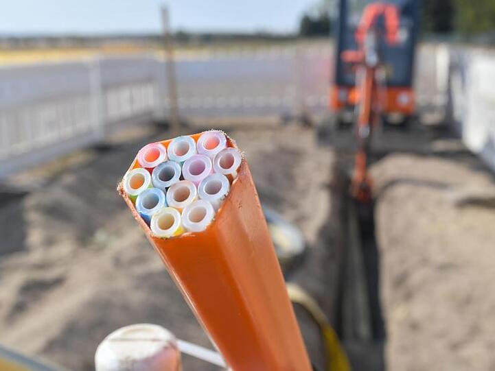 Farbige Leerrohre, in die später Glasfaserkabel verlegt werden, ragen aus dem Graben einer Baustelle.