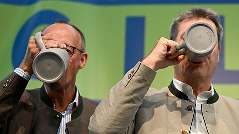 CDU-Chef Friedrich Merz (l) und Bayerns Ministerpräsident Markus Söder (CSU) trinken beim Politischen Frühschoppen Gillamoos auf der Bühne aus Bierkrügen.