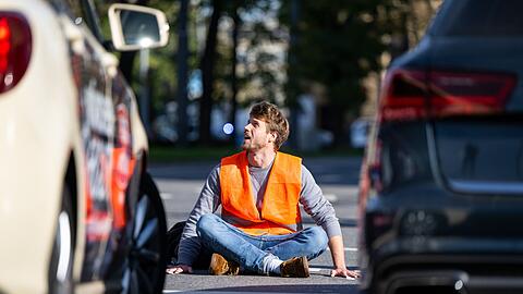 Ein Klimaaktivist sitzt auf der Fahrbahn und blockiert die Straße.