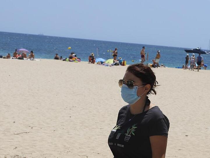 Eine junge Frau mit einer Schutzmaske an einem Strand.