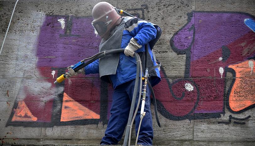 Ein Arbeiter mit Schutzhelm entfernt das Graffito von der Ludwigsbrücke.