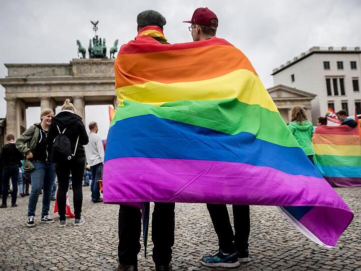 Eingehüllt in eine Regenbogenflagge, steht ein homosexuelles Paar vor dem Brandenburger Tor in Berlin. Experten gehen von Tausenden Fällen pro Jahr in Deutschland aus, in denen versucht wird, Homosexuelle mit fragwürdigen Therapien zu "heilen".
