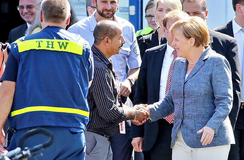Bundeskanzlerin Angela Merkel (CDU, r) besucht eine Flüchtlingsunterkunft in Heidenau (Sachsen) und spricht mit einem der Helfer.