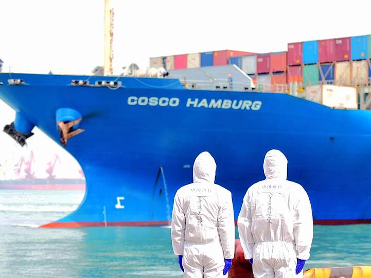 Zwei Hafenmitarbeiter in Qingdao beobachten den Containerfrachter "Cosco Hamburg".