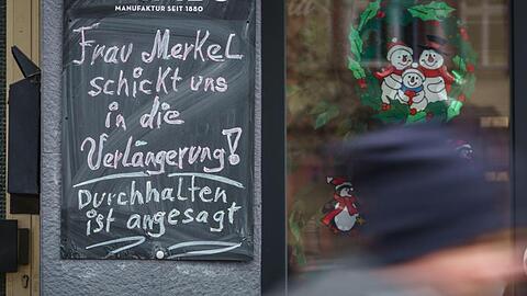 "Frau Merkel schickt uns in die Verlängerung! Durchhalten ist angesagt!" steht auf einer Tafel neben einem geschlossenen Geschäft im hessischen Friedberg.