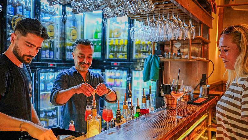 Vor drei Jahren eröffnete Yilmaz Demir (Mitte) die Boazn in einem ehemaligen Klohäuschen an der Ludwigsbrücke. Mittlerweile ist die Bar, die zugleich Tanzbar ist, vom Isarufer kaum mehr wegzudenken. Gerade mixt Demir die neue Spritzvariante "GrapefruitSpritz" für seine Stammgästin Katinka Behnke (rechts). Vor drei Jahren eröffnete Yilmaz Demir (Mitte) die Boazn in einem ehemaligen Klohäuschen an der Ludwigsbrücke. Mittlerweile ist die Bar, die zugleich Tanzbar ist, vom Isarufer kaum mehr wegzudenken. Gerade mixt Demir die neue Spritzvariante "GrapefruitSpritz" für seine Stammgästin Katinka Behnke (rechts).