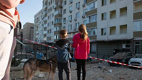 Kriegsalltag: Kinder schauen in Kiew auf ein bei russischen Raketenangriffen beschädigtes Gebäude.