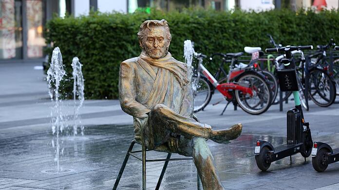 Hier sitzt Helmut Dietl - zwischen Wasserspiel und E-Scootern.
