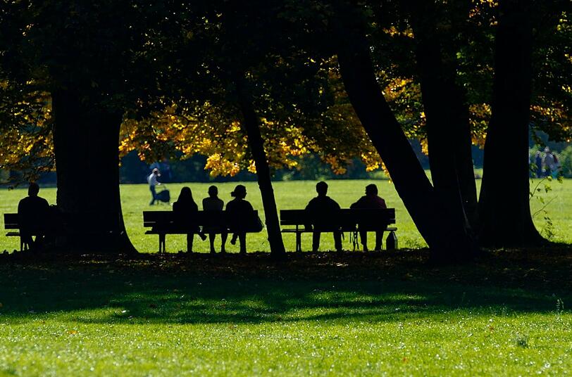 Menschen sitzen am Dienstag auf den Parkbänken im Englischen Garten.