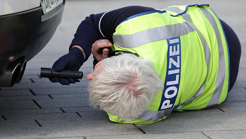 Ein Polizist leuchtet bei einer Kontrolle mit einer Taschenlampe in den Auspuff eines Fahrzeuges. (Symbolbild)