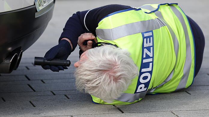 Ein Polizist leuchtet bei einer Kontrolle mit einer Taschenlampe in den Auspuff eines Fahrzeuges. (Symbolbild)