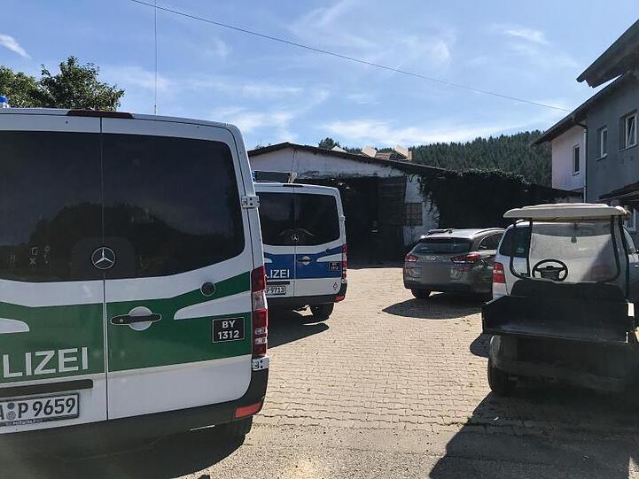 Polizeifahrzeuge stehen neben anderen Fahrzeugen auf einem Hof vor einem Stall im Allgäu. Foto: Benjamin Liss