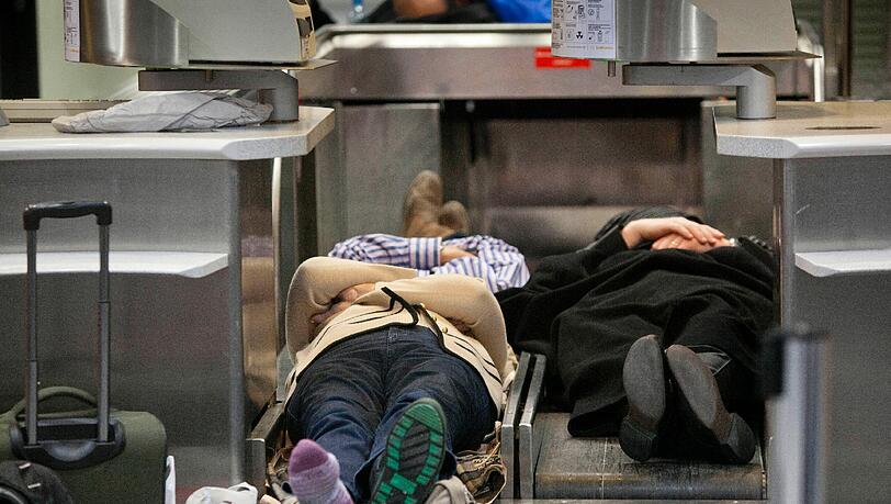 Nicht die beste Art eine Nacht zu verbringen: Gestrandete Passagier schlafen am Frankfurter Flughafen auf Gepäckbändern (Archivbild). Nicht die beste Art eine Nacht zu verbringen: Gestrandete Passagier schlafen am Frankfurter Flughafen auf Gepäckbändern (Archivbild).