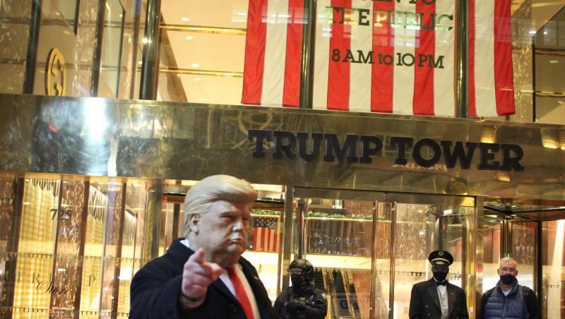 Ein Mann mit einer Trump-Maske in der Hand gestikuliert vor dem Trump Tower, der von einem Polizisten einer Spezialeinheit des NYPD auf der 5th Avenue in Manhattan am Vorabend der Präsidentschaftswahlen gesichert wird.